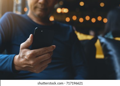 Young Man, Freelance Using Mobile Smart Phone In Coffee Shop Or Cafe With Colorful Light Bokeh Background, Close Up, Dark Tone And Background. Modern Life Style Concept