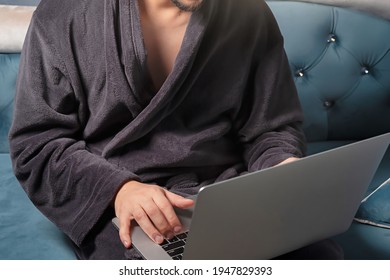 Young Man Freelancer In A Dressing Gown Working From Home On A Laptop