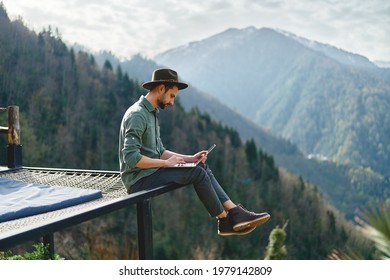 Young man freelancer traveler wearing hat anywhere working online using laptop and enjoying mountains view - Shutterstock ID 1979142809
