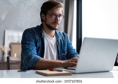Young man freelancer using laptop studying online working from home, happy casual guy typing on notebook
