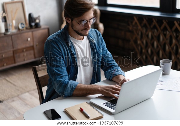 Young man freelancer\
using laptop studying online working from home, happy casual guy\
typing on notebook