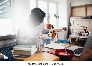 Young Man Freelancer Working From His Home. Cuddling With His Dog