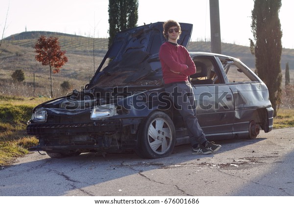 Young man\
in front of a destroyed car after\
accident