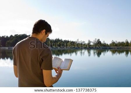 Young man in front of lake reading the Bible (King James Version)
