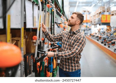 a young man in a gardening equipment store chooses an electric trimmer for mowing lawn grass.