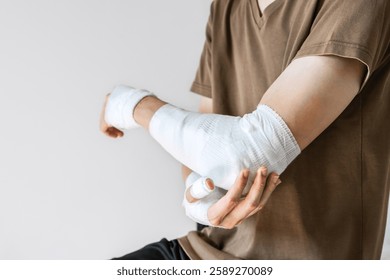 Hombre joven con vendaje de gasa envuelto alrededor de su brazo lesionado. Hombre con la mano envuelta en vendaje médico sobre fondo blanco. Primeros auxilios, tratamiento del brazo después de una lesión por accidente. Copiar espacio