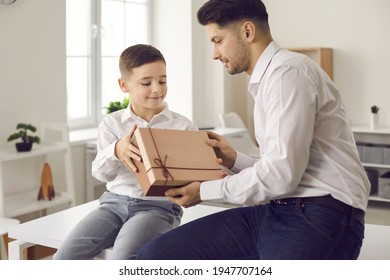 Young Man Getting Birthday Gift And Thanking His Little Son For Surprise. Child Giving Present Box To His Dad And Wishing Him Happy Father's Day. Exchanging Presents On Special Family Occasion Concept