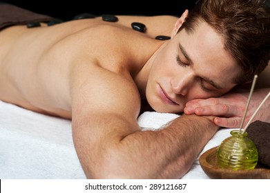 Young Man Getting A Stone Massage At Spa