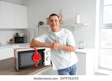 Young man with gift microwave oven in kitchen - Powered by Shutterstock