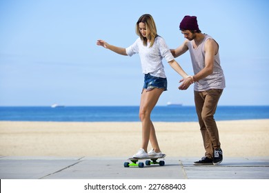 Young man gives his girlfriend her first skateboarding lesson on a seaside boulevard, during a lovely, calm summer afternoon. - Powered by Shutterstock