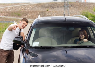 Young man giving directions to a woman driver standing talking to her through the passenger window and pointing out the route with his hand - Powered by Shutterstock