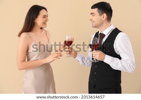 Young man giving his girlfriend glass of wine on beige background