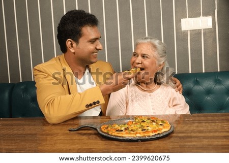 Young man giving pizza to a senior lady in Restaurant.