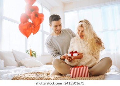 Young man giving present to his girlfriend at home. Beautiful young couple at home celebrating Valentine's Day. Romantic day. - Powered by Shutterstock