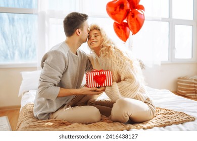 Young man giving present to his girlfriend at home. Beautiful young couple at home celebrating Valentine's Day. Romantic day. - Powered by Shutterstock