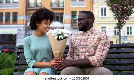 Young Man Giving White Flower Bouquet To Woman Sitting Bench, First Awkward Date