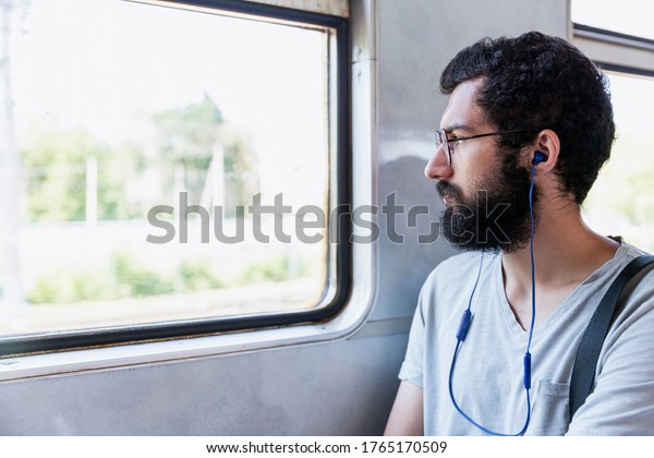 A\
young man with glasses, headphones and a beard sits in a train car\
and listens to music. Tourism and travel.\
Close-up.