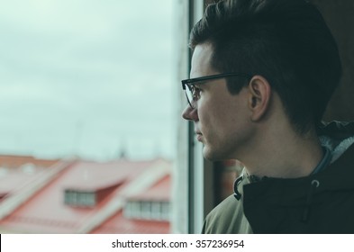 Young man in glasses looking through a window - Shutterstock ID 357236954