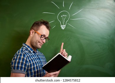 A young  man with glasses is reading a book, an idea comes to mind on the background of a blackboard with a chalked light bulb.
