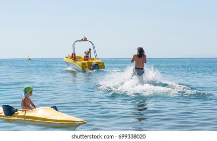 Young Man Glides On Water Skiing On The Waves On The Ocean. Healthy Lifestyle. Positive Human Emotions. Smiling Little Baby Boy In Green Baseball Cap Kayaking At Tropical Ocean Sea In The Day Time. 