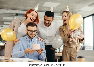 Young man is going to blow candles on cake and make a wish while celebrating birthday with colleagues. Colleagues celebrating a birthday in the office - Powered by Shutterstock