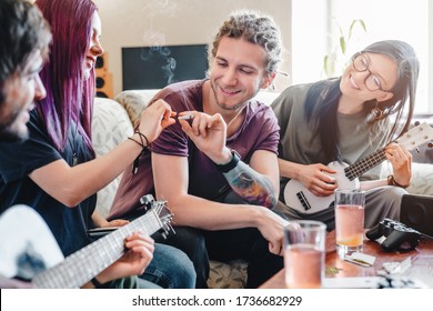 Young man going to smoke joint rolled with cannabis while relaxing with friends at home