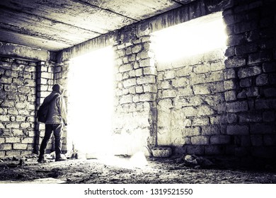 Young Man Goint To Bright Light. Abandoned Unfinished Construction And A Young Man Going To The Doorway. Bright Light Coming Through A Window Frame And A Doorway.