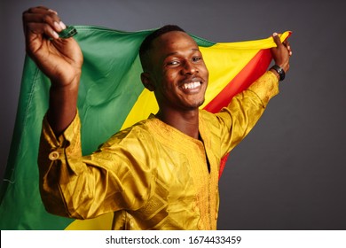 Young man in gold national clothes smiling into the camera and posing with Congo Flag isolated in gray Background.