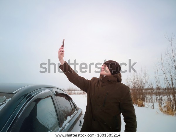 A young man got lost in
a car in winter and is trying to catch the mobile network after
getting out of the car. Concept of winter road travel, road search,
navigation.