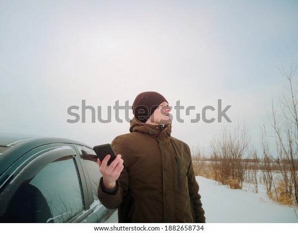 A young man got lost in\
a car in winter and is trying to catch the mobile network after\
getting out of the car. Concept of winter road travel, road search,\
navigation.