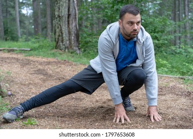 Young Man In Gray Sweat Suit Preparing For Exercise. Stretching Legs Warming Up.