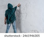 A young man in a green hoodie is spraying graffiti on a wall. Scene is rebellious and edgy, as the act of graffiti is often associated with vandalism and defiance of authority