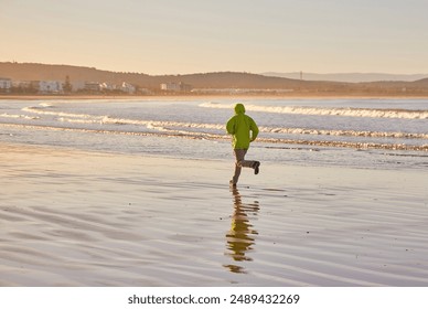 A young man in a green jacket enjoys a run along the Essaouira coastline in Morocco, where the ocean breeze invigorates the seaside atmosphere - Powered by Shutterstock