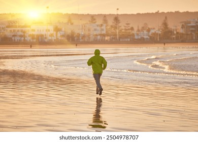 A young man in a green jacket enjoys a run along the Essaouira coastline in Morocco, where the ocean breeze invigorates the seaside atmosphere - Powered by Shutterstock