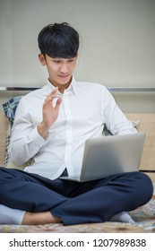 Young Man Greeting Shi Friends Via Laptop Web Cam While Sitting On Bed.