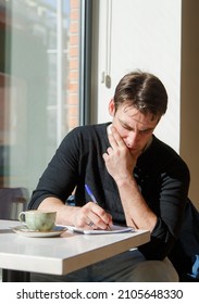  Young Man In A Grey Jacket Writing Something In Note Book While Taking A Coffee At The Bar 