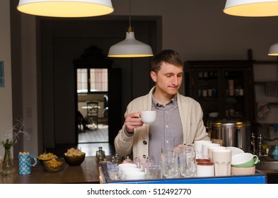 Young man in grey shirt with cup of coffee is looking at the coffee machine