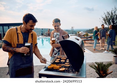 Young man grilling food while having backyard poolside barbecue party with his friends.  - Powered by Shutterstock