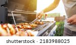 Young man grilling some kind of meats on the gas grill during lovely summer time, food concept