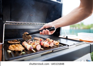 Young man grills some kind of marinated meat and vegetable on gas grill during summer time
