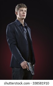 Young Man With Gun. Dark Red Background. Standing Portrait.