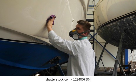 A young man (guy) is a specialist in cleaning the yacht, in a respirator and using a spray. Concept from: Professional, Specialist, Cleaning, Service, Preparation.
