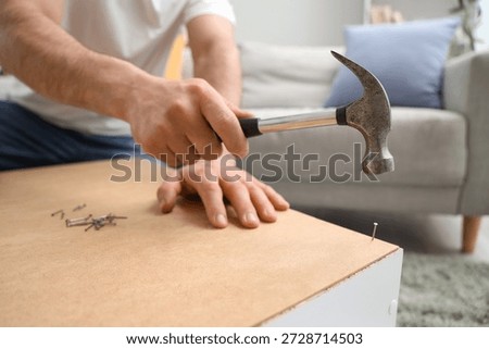 Young man with hammer assembling shelf unit at home, closeup