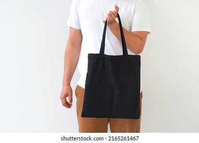 Young Man Hand Holding Black Canvas Tote Bag On White Background. Reusable Eco Bag For Shopping. Eco Friendly Concept. Mockup For You Designs.