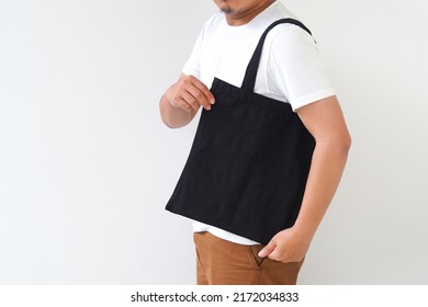 Young Man Hand Holding Black Canvas Tote Bag On White Background. Reusable Eco Bag For Shopping. Eco Friendly Concept. Mockup For You Designs.