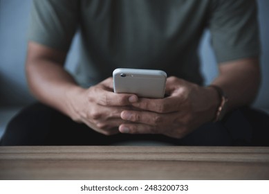 Young man hand holding cell phone on the sofa in the living room. He was reading and answering emails and shopping online on weekends at home. - Powered by Shutterstock