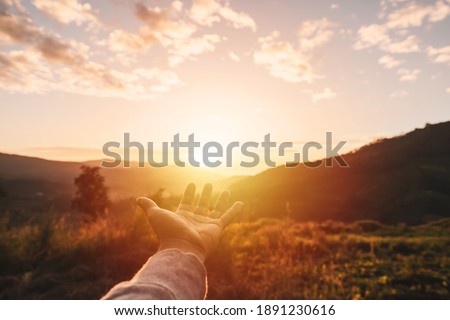 Young man hand reaching for the mountains during sunrise and beautiful landscape