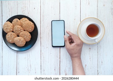  young man hand using smart phone with tea and cookies on table 