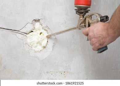 Young man hand using spray gun and filling hole with construction foam in concrete wall where was old outlet. Closeup. Repair work of home. Renovation process. Side view.