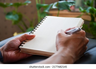 Young Man Hand Writing Blank Notebook On Wooden Table Hill In The Morning Tree Background
